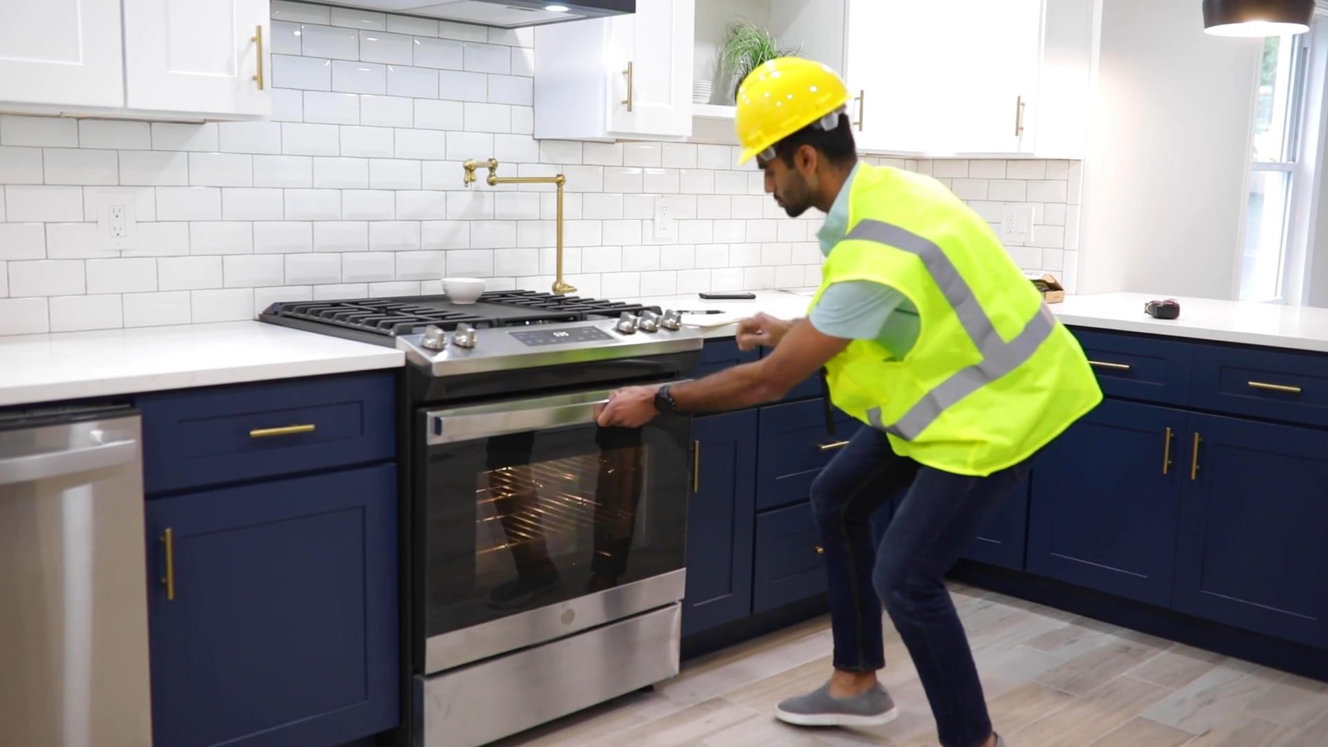 A home services professional in a hard hat and safety vest inspecting a gas range in a residential kitchen