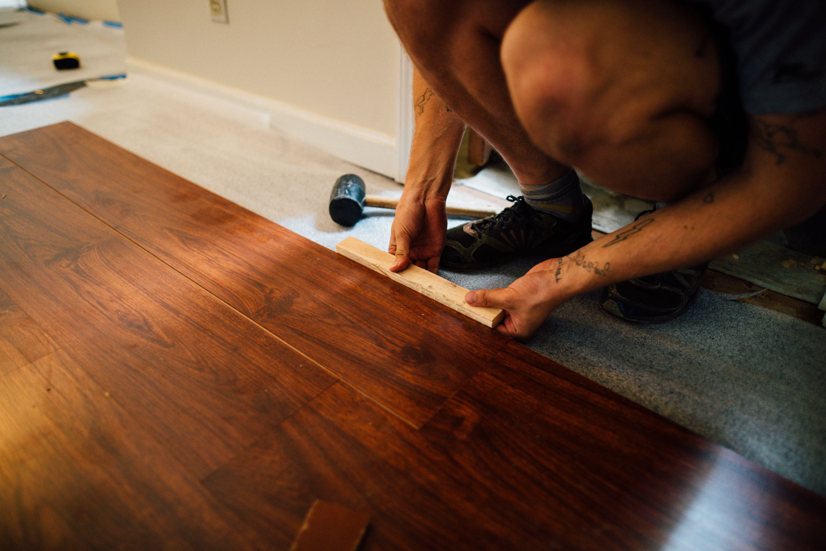 A worker laying wooden laminate flooring with a mallet during a home renovation